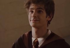 a young man wearing a harry potter robe and tie looking at the camera with an intense look on his face