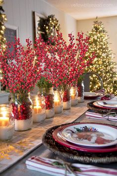 the table is set for christmas dinner with red berries in mason jars and lit candles