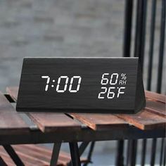 an alarm clock sitting on top of a wooden table next to a chair and brick wall