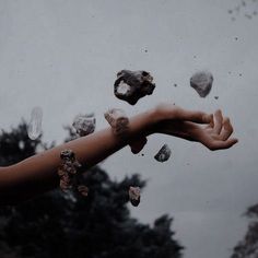 a person's hand reaching for rocks in the air with trees and sky in the background