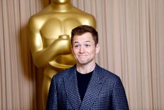 a man standing in front of an oscar statue wearing a blue suit and black shirt