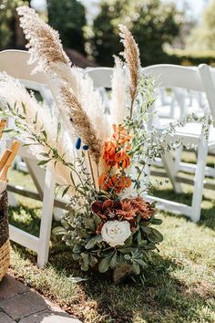 an outdoor ceremony setup with white chairs and pamodia in vases on the grass