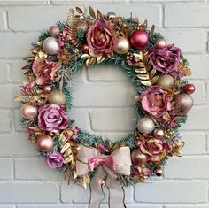 a wreath with pink and gold ornaments hanging on a wall next to a brick wall