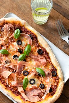 a pizza sitting on top of a white plate next to a fork and glass filled with olives