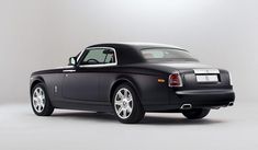 a black rolls royce parked in front of a white wall