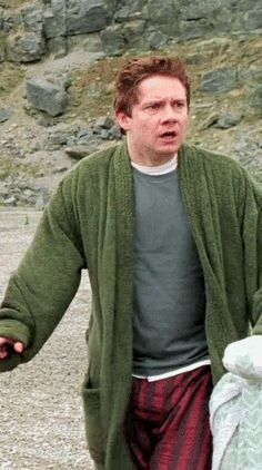 a man in green sweater and plaid pants holding a white teddy bear on the beach