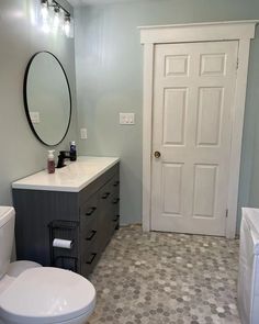 a white toilet sitting next to a sink in a bathroom under a large round mirror