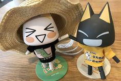 two small figurines are sitting next to each other on a wooden table, one is wearing a hat and the other has a yellow t - shirt