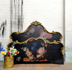 a bed with flowers painted on it next to a potted plant and brick wall