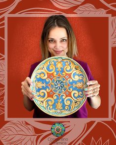 a woman holding up a decorative plate in front of a red background with an ornate design