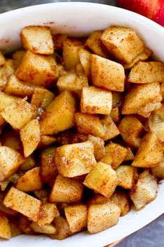 a white bowl filled with apples and cinnamon on top of a table next to an apple