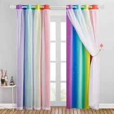 rainbow colored curtains hanging in front of a window with white walls and wooden flooring