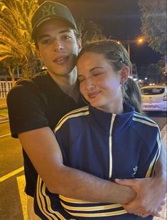 a man and woman hugging each other on the street at night with palm trees in the background