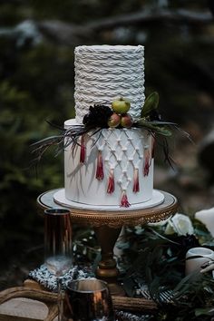 a three tiered cake with white icing and red decorations on a gold stand