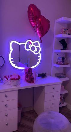 a hello kitty neon sign on a desk with some balloons in the corner and a cake