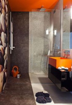 an orange and black bathroom with rocks on the wall, shower stall and sink area