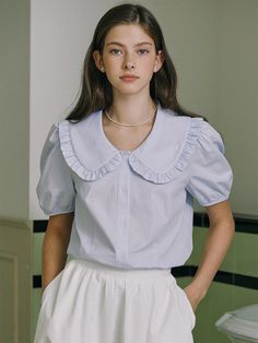 This product is a ruffle collar stripe blouse that exudes a combination of vintage charm and contemporary fashion. It is characterized by its distinctive ruffled collar and puff sleeves, with a subtle striped pattern running throughout the fabric. The blouse's button-down front and tailored fit offer a polished look, while the lightweight material provides comfort and breathability. - The ruffle collar gives this blouse a playful and feminine aesthetic.- Puff sleeves add volume and a whimsical touch to the sophisticated design.- Its vertical striped pattern elongates the silhouette and adds a classic detail.- Crafted with a comfortable and breathable fabric, this blouse is suitable for all-day wear in various settings. Frilly Collar Blouse, Puff Sleeve Button Up, Statement Collar Blouse, Collar Blouse Outfit, Shraddha Srinath, Blouse With Puff Sleeves, Ruffle Collar Shirt, Dark Blue Blouse, Blue Ruffle Top