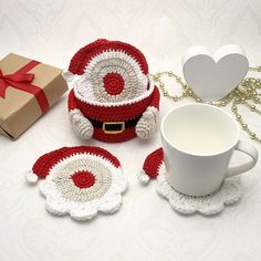 a crocheted santa clause hat and two mug cozyies next to a gift box