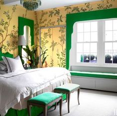 a bedroom with green walls and white bedding, windows, and bench in the corner