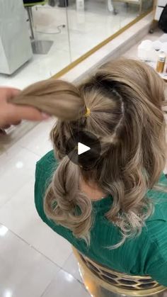 a woman sitting at a table with her hair in a pony tail style braid and wearing a green shirt