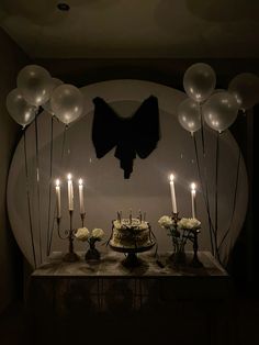 a table topped with a cake covered in white frosting surrounded by balloons and candles