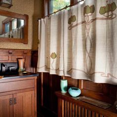 a kitchen with wooden cabinets and a window covered in curtained drapes next to a sink