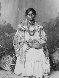 an old black and white photo of a woman in native garb sitting on the ground