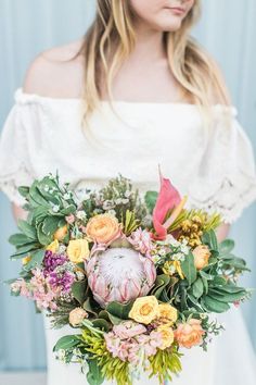 a woman holding a bouquet of flowers in her hands and wearing an off the shoulder white dress