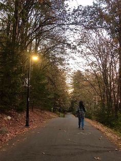 a person walking down the road in front of some trees and street lights at dusk