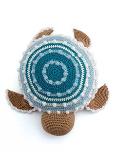 a crocheted turtle pillow sitting on top of a white surface with blue and brown accents