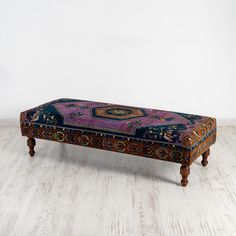 a bench with an intricately decorated design on the top and bottom, sitting on a white wooden floor