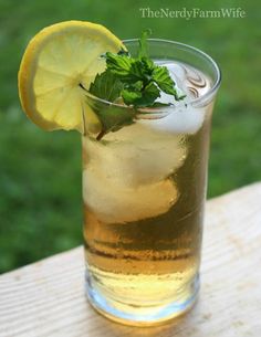 a glass filled with lemonade and mint on top of a wooden table next to grass