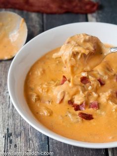 a spoon full of cheese soup with bacon on the side and another bowl in the background