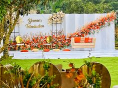 an outdoor wedding setup with orange and white flowers on the grass, surrounded by greenery