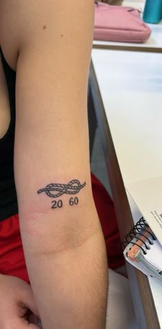 a woman's arm with a tattoo on it that reads 20 60 and has a ball of yarn in the middle