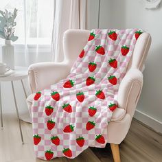 a pink and white checkered blanket with red strawberries on it sitting in a chair