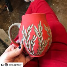 a woman is holding a red mug with leaves on it