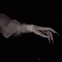 a woman's hand with long nails and white dress in the dark at night