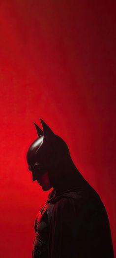 a man dressed as batman standing in front of a red background