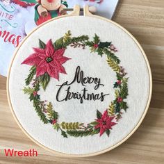 a merry christmas wreath with poinsettis and holly on the hoop next to a book