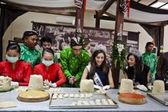 a group of people standing around a table with cakes on top of it and wearing masks