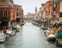 several boats are parked along the side of a canal in an old city with tall buildings