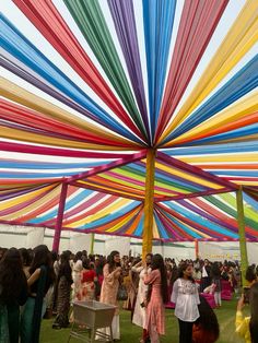 a group of people standing under a multi colored canopy on top of a grass covered field