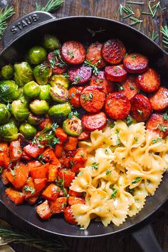 a skillet filled with pasta, vegetables and sausages on top of a wooden table