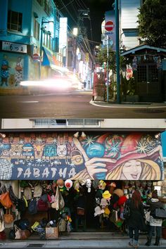 people are standing in front of a store with graffiti on the wall and below it