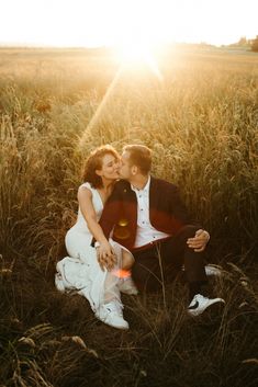 a newly married couple kissing in the middle of a field with the sun behind them