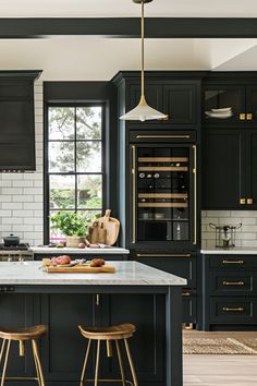 a large kitchen with black cabinets and gold accents on the counter tops, along with two stools