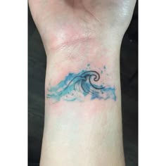 a small wave tattoo on the wrist, with blue water splashing down it's side