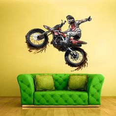 a person on a dirt bike jumping in the air over a green couch and yellow wall