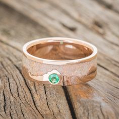 a wedding band with an emerald stone in the center sits on a wooden plank surface